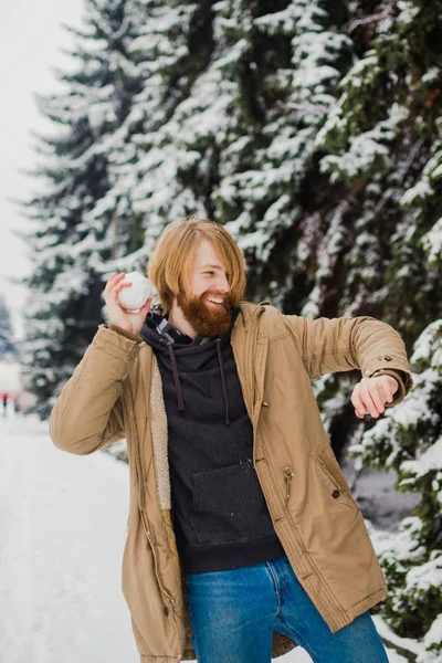 Young Caucasian boy in love with a beard date in the open air in the winter park against the background of a snowy conifer tree play snowballs, throw snow, hang themselves and play in the winter games.