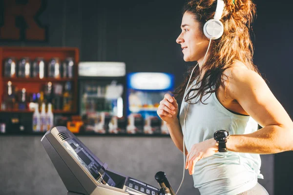 主题是体育和音乐 一个漂亮的充气女人在健身房里跑步 在她的头上是一个大的白色耳机 女孩听音乐在心脏锻炼减肥 — 图库照片