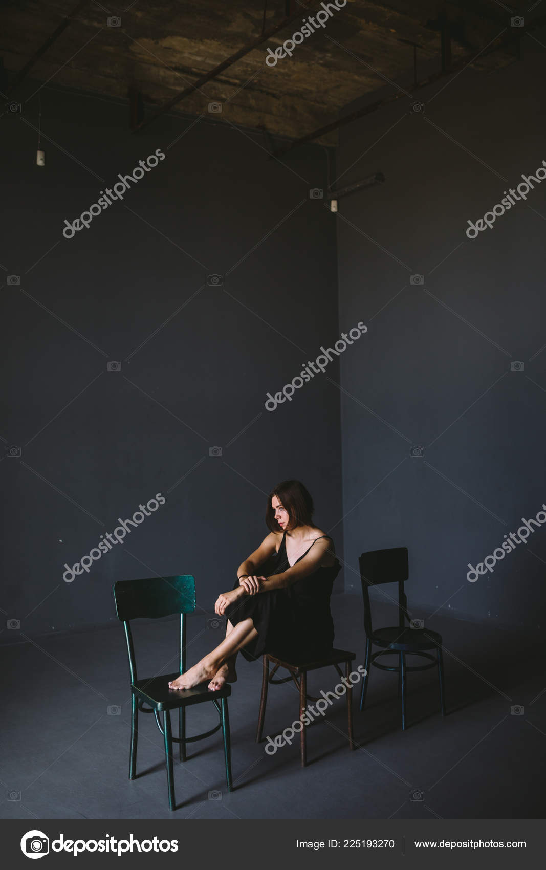 社会主题女性孤独痛苦痛苦虐待男性暴力家庭一个穿着黑色衣服的年轻美丽的白人妇女坐在黑暗的大房间里的三把椅子上斯拉奇和绝望