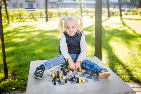 Funny Caucasian baby girl blonde does not want learn, does not want to school, want to play, laugh and indulge. child with hair ponytail sits table legs forward, spread out, mess, tabletop logic game.