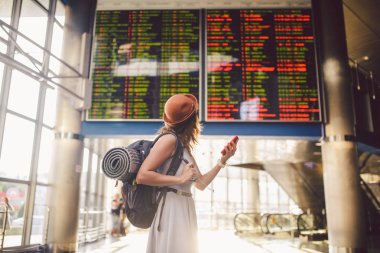 Tema seyahat ve tranosport. Güzel genç kafkas kadın elbise ve tren istasyonuna veya kırmızı telefon tutarak bir zamanlama seyir terminal içinde duran sırt çantası iletişim teknolojisini kullanır.