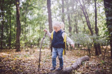 Tema açık hava etkinlikleri doğada. Komik küçük beyaz sarışın kızı ormanın içinde büyük bir sırt çantası ile engebeli arazide hiking yürür yürür. Baston kullanır