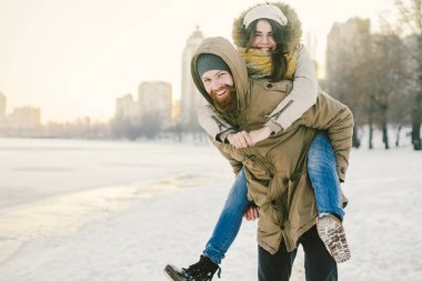 Tema yeni yıl Noel ruh kış kar Tatil Sevgililer günü. Kafkas çift aşıklar neşe, kahkaha Şehir Parkı suya kandırmak. adam kadının omuzlarında sırt çantası tutar.