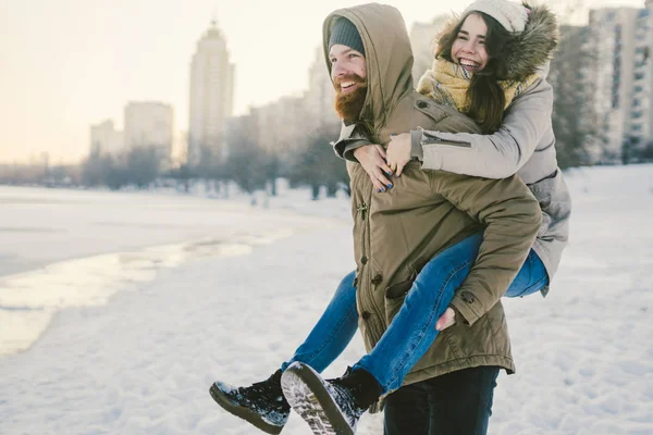 Tema yeni yıl Noel ruh kış kar Tatil Sevgililer günü. Kafkas çift aşıklar neşe, kahkaha Şehir Parkı suya kandırmak. adam kadının omuzlarında sırt çantası tutar.