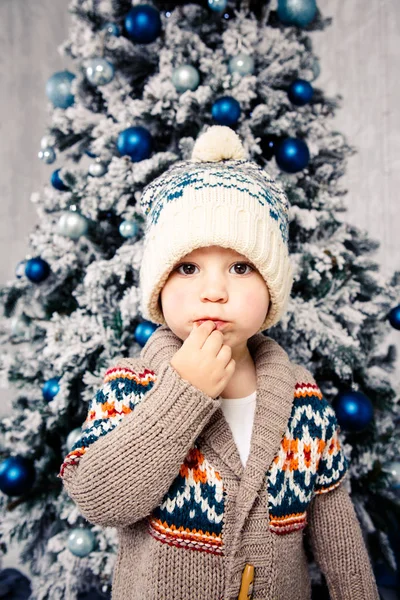 Christmas theme and children. Little Caucasian boy child in a warm hat and sweater posing, eating sweetness, dirty face. Christmas morning. New Year\'s holidays.