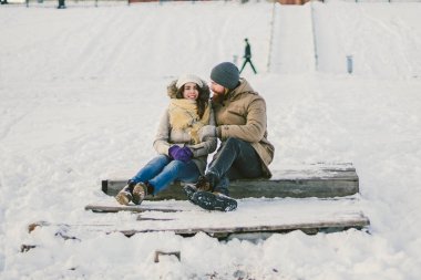 Bir sakallı bir adam sevgi dolu çift gençler ve beyaz bir kadın oturuyor bir ahşap merdiven üzerinde kışın karda Sevgililer günü tarihi Noel sarılma ve mutlu.