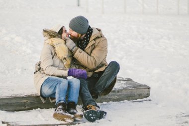 Bir sakallı bir adam sevgi dolu çift gençler ve beyaz bir kadın oturuyor bir ahşap merdiven üzerinde kışın karda Sevgililer günü tarihi Noel sarılma ve mutlu.