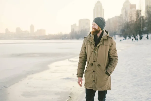 クローズ アップ白人若い男性赤い髪とひげ 帽子と雪を凍結する湖を背景に冬モデルをポーズ公園コート — ストック写真
