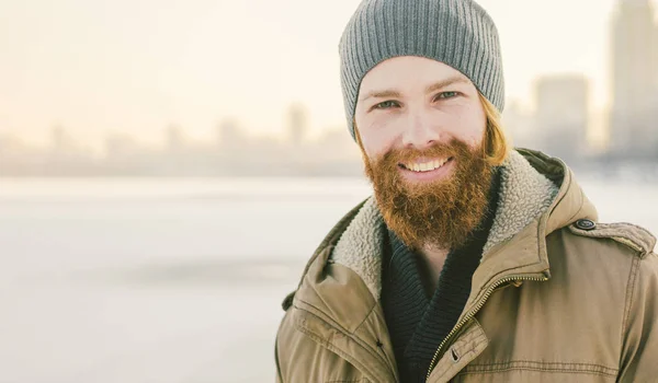 クローズ アップ白人若い男性赤い髪とひげ 帽子と雪を凍結する湖を背景に冬モデルをポーズ公園コート — ストック写真