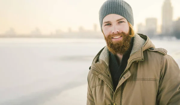 クローズ アップ白人若い男性赤い髪とひげ 帽子と雪を凍結する湖を背景に冬モデルをポーズ公園コート — ストック写真