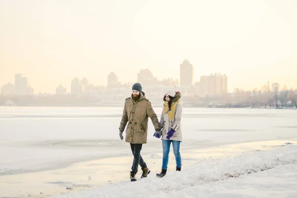主题圣诞节假期冬季新年 年轻的时尚的白种人爱的夫妇异性行走在一个冰冻的岸边 情人节在冬天在日落 爱情与浪漫主题 — 图库照片