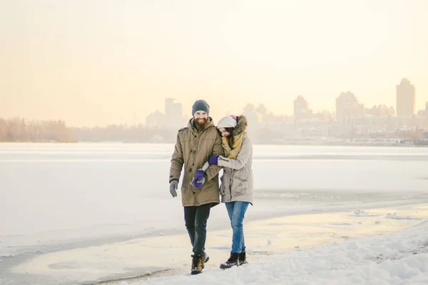 Theme Christmas holidays winter new year. Young stylish Caucasian loving couple Heteresexual walking on the shore of a frozen lake. Date. Valentines Day in winter at sunset. Love and Romance Theme.