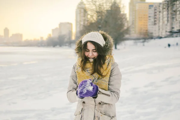 スノース マイルとニットの帽子とマフラーの上に立って美しい若い白人女性の肖像画冬背景し 幸福紫手袋が雪玉を彫る — ストック写真