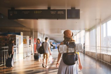 Tema seyahat toplu taşıma. elbise ve şapka sırt çantası arkasında arkada ayakta ve ekipman yatınca, kamp genç kadın mat yalıtım çetele Havaalanı İstasyonu güneşli gün programa benziyor.