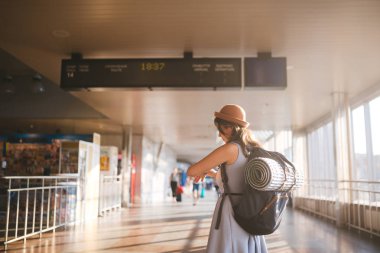 Tema seyahat toplu taşıma. elbise ve şapka sırt çantası arkasında arkada ayakta ve ekipman yatınca, kamp genç kadın mat yalıtım çetele Havaalanı İstasyonu güneşli gün programa benziyor.