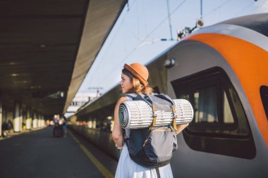 Tema ulaşım ve seyahat. Tren İstasyonu platformu yakınındaki sırt çantası seyahat mat uykulu havalarda elbise ve şapka yaz aylarında ile tren sırt tren arka plan ayakta beyaz kadın.