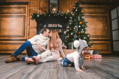 Tema aile tatil yeni yıl ve Noel. Genç beyaz aile anne baba oğlu 1 yıl sit ahşap zemin şömine Noel ağacı Noel akşamı yakınındaki. Sürüngenler arka plan veliler öğrenme bebek yürüyüşü