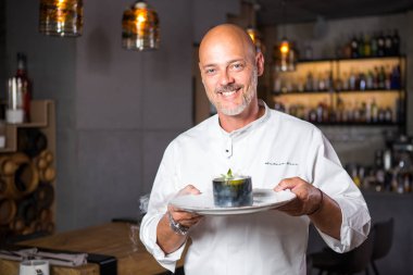 Yakışıklı İtalyan adam kel beyaz üniforma şef onun elinde kazma dişli bir gülümseme ile tatlı bir tabak poz bir restoranda bir sakallı.