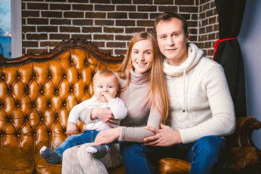 Tema yeni yıl ve Noel tatili aile ortamı içinde. Ruh kutlamak beyaz genç anne baba ve oğlu 1 yaşında oturup Noel ağacı yakınındaki oturma odasında evde deri kahverengi kanepe.