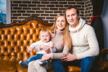 Tema yeni yıl ve Noel tatili aile ortamı içinde. Ruh kutlamak beyaz genç anne baba ve oğlu 1 yaşında oturup Noel ağacı yakınındaki oturma odasında evde deri kahverengi kanepe.