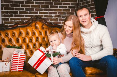 Tema yeni yıl ve Noel tatili aile ortamı içinde. Ruh kutlamak beyaz genç anne baba ve oğlu 1 yaşında oturup Noel ağacı yakınındaki oturma odasında evde deri kahverengi kanepe.