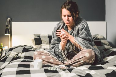 Mevsimlik soğuk, burun akıntısı grip virüsü enfeksiyonu temasıdır. Genç beyaz bir kadın kaydırma battaniye oturan ev yatak odası yatak chill ısı yüksek sıcaklığı. Bardak içki hapları sezon gribi blister.