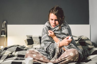 Mevsimlik soğuk, burun akıntısı grip virüsü enfeksiyonu temasıdır. Genç beyaz bir kadın kaydırma battaniye oturan ev yatak odası yatak chill ısı yüksek sıcaklığı. Bardak içki hapları sezon gribi blister.