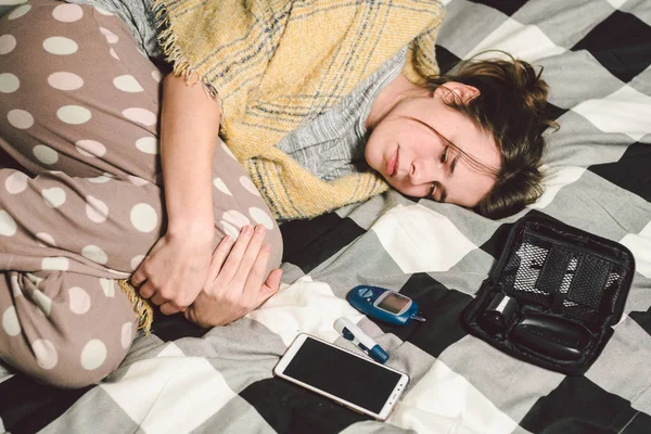Theme diabetes. young caucasian woman at home in the bedroom on the bed uses the technology of the device for measuring blood glucose, glucometer test strips high sugar level disease.