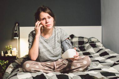 Konu yüksek tansiyon hipertansiyon hastalığı. Güzel ve genç birbayan otomatik tonometer yatak odasında yatağın üstüne basınç ev denetlemek için kullanır. Bir kadın yardım isterse, bir ambulans 911'i ara.