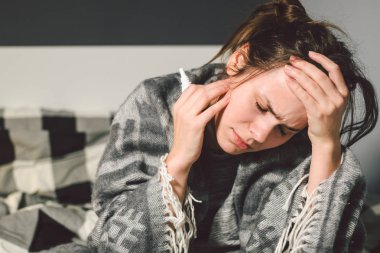 Denek hastalık ve tedavi. Kafkasyalı genç bir kadın yatak odasında yüksek ateşi olan bir battaniyeye sarılmış, ateşi baş ağrısına neden oluyor, sinüzit için burun içine ilaç koyuyor.