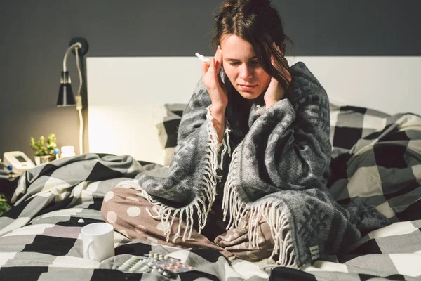 Sujeto enfermedad y tratamiento. joven mujer caucásica se sienta en casa dormitorio cama envuelta en manta corporal con fiebre alta, fiebre sostiene fuerte dolor de cabeza detrás de la cabeza, utiliza medicamentos de gota en la nariz para la sinusitis — Foto de Stock