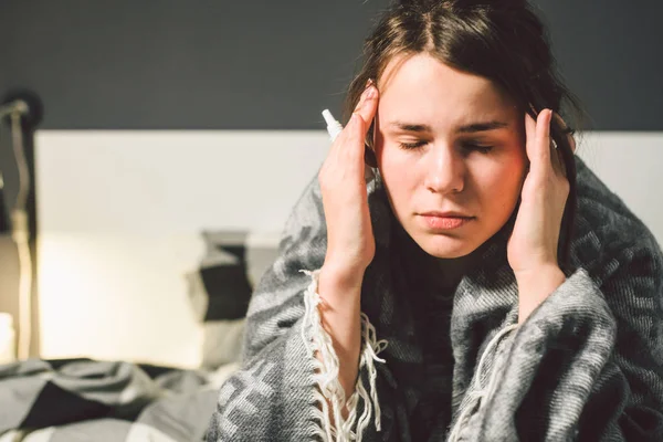 Sjukdom och behandling. ung kaukasisk kvinna sitter hemma sovrum säng insvept i kroppen filt med hög feber, feber håller stark huvudvärk bakom huvudet, använder droppe medicin i näsan för bihåleinflammation — Stockfoto