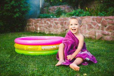 Yaz tatil tema. Kuru bir havlu kırmızı yüzme şort olmak yok, yuvarlak bir şişme renkli havuz yakınındaki çimenlerin üzerinde bir evin arka bahçesinde oynarken küçük 3 yaşındaki beyaz çocuk sarılmış.