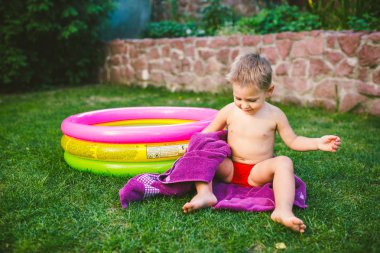 Yaz tatil tema. Kuru bir havlu kırmızı yüzme şort olmak yok, yuvarlak bir şişme renkli havuz yakınındaki çimenlerin üzerinde bir evin arka bahçesinde oynarken küçük 3 yaşındaki beyaz çocuk sarılmış.
