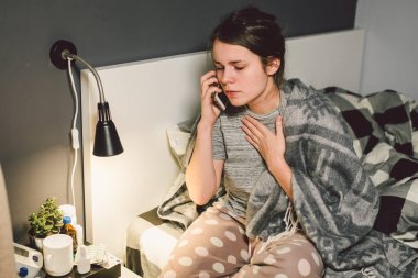 respiratory diseases and home remedies. young woman sick with cold sitting bedroom on bed holding throat sadness emotion. Sore throat man takes pills. Call phone, ask for help doctor. Call ambulance.