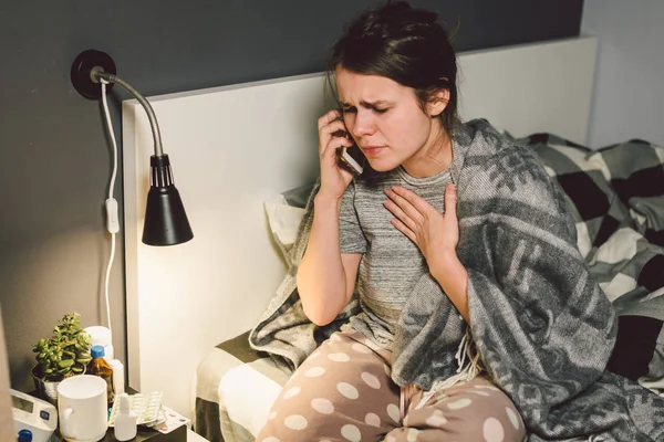 respiratory diseases and home remedies. young woman sick with cold sitting bedroom on bed holding throat sadness emotion. Sore throat man takes pills. Call phone, ask for help doctor. Call ambulance.