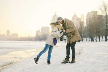 Tema aşk ve doğa tarihi. Genç beyaz heteroseksüel çift erkek ve kız kışın donmuş bir gölün yakınında kışın sıcak kucaklama eşarp öp. Sakallı adam kadın sarılma. Sevgililer günü tatil.
