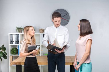 Tema işletme, ekip çalışması ve ortaklıklar. Bir grup genç insan, üç kişi, resmi kıyafet tablosunda yakın bir ofiste durmak, belgelerle çalışmak, praks işaret sözleşme yapmak.