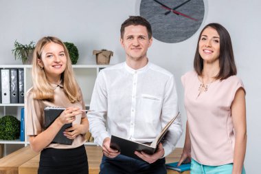 Tema işletme, ekip çalışması ve ortaklıklar. Bir grup genç insan, üç kişi, resmi kıyafet tablosunda yakın bir ofiste durmak, belgelerle çalışmak, praks işaret sözleşme yapmak.