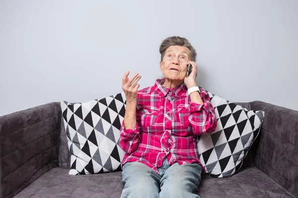 主题老人使用技术 成熟快乐的喜悦微笑活跃的灰发白种人皱纹妇女坐在家里的客厅在沙发上 用手机 打电话和交谈 — 图库照片