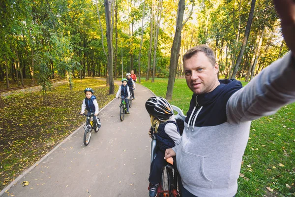The theme family sports outdoor recreation. large family Caucasian 6 people mom dad and 4 children three brothers and sister ride bicycles in park on bicycle path. Father holds camera makes photo.