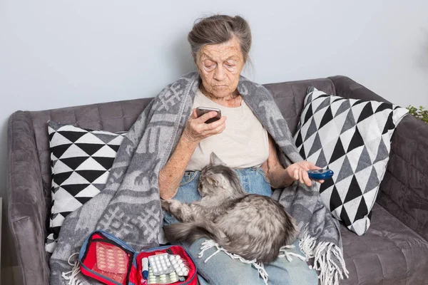 Theme old man and diabetes. older Caucasian woman with gray hair wrinkle home on sofa measures glucose level blood with help medical device using blood glucose meter. Hand ear phone call ambulance.