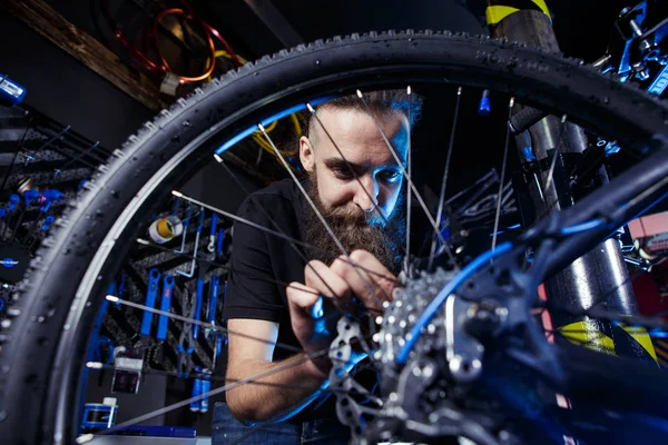 Subject profession. Young stylish caucasian male with a beard at work is repairing a bicycle. Bike shop, service and repair of bikes. Look at the wheel.