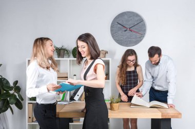 Konu iş, takım çalışması ve müzakerelerin ofiste. 4 beyaz insanlar odasında belgelerle çalışma grubu. İki genç kadın patron şirket çalışanları fonunda poz.