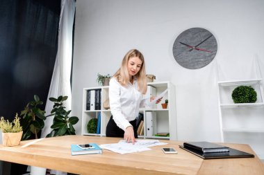 Tema iş kadını iş başında. Güzel genç kafkas kadın iş adamı çalışma ayakta tablo yakınındaki ofiste denetler kağıt üzerinde düzenlemeler finansal grafikler.