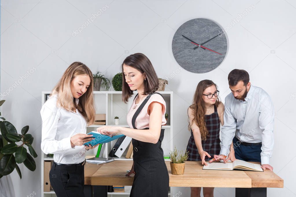 Subject business, teamwork and negotiations in the office. A group of 4 Caucasian people working with documents in the room. Two young women bosses posing against the backdrop of company employees.