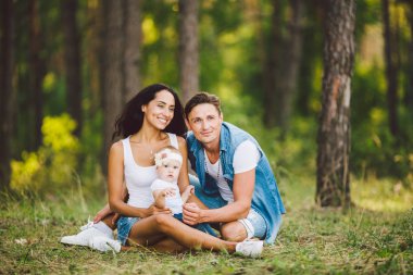 Tema aile açık rekreasyon orman park alanında. Genç güzel şık beyaz aile küçük çocuk kızı bir yaşında ile oturup iğne yapraklı orman çim üzerinde yaz gün batımında.