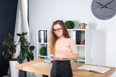 Bir office odada bir masa yakınındaki bir ofiste uzun saçlı ve gözlüklü sürtünme ile genç beyaz bir kadın portresi duruyor. Üniversite öğrencisi kız. Öğrenme konu adam.