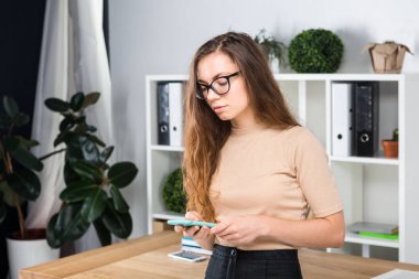 Bir office odada bir masa yakınındaki bir ofiste uzun saçlı ve gözlüklü sürtünme ile genç beyaz bir kadın portresi duruyor. Üniversite öğrencisi kız. Öğrenme konu adam.