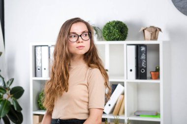 Bir office odada bir masa yakınındaki bir ofiste uzun saçlı ve gözlüklü sürtünme ile genç beyaz bir kadın portresi duruyor. Üniversite öğrencisi kız. Öğrenme konu adam.